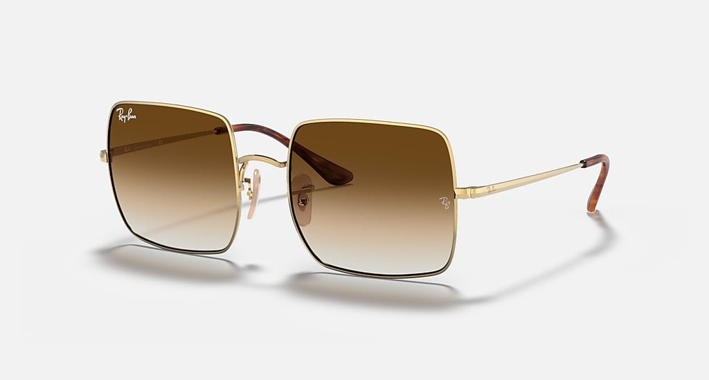 The Ray-Ban 1971 Square sunglasses feature clear gradient brown lenses, oversize square metal frames with gold detail, and thin temples, shown against a plain light background.