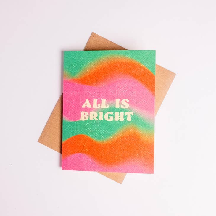 The All Is Bright greeting card by Daydream Prints features wavy orange, pink, and green hues with "ALL IS BRIGHT" on the front and comes with a recycled envelope.