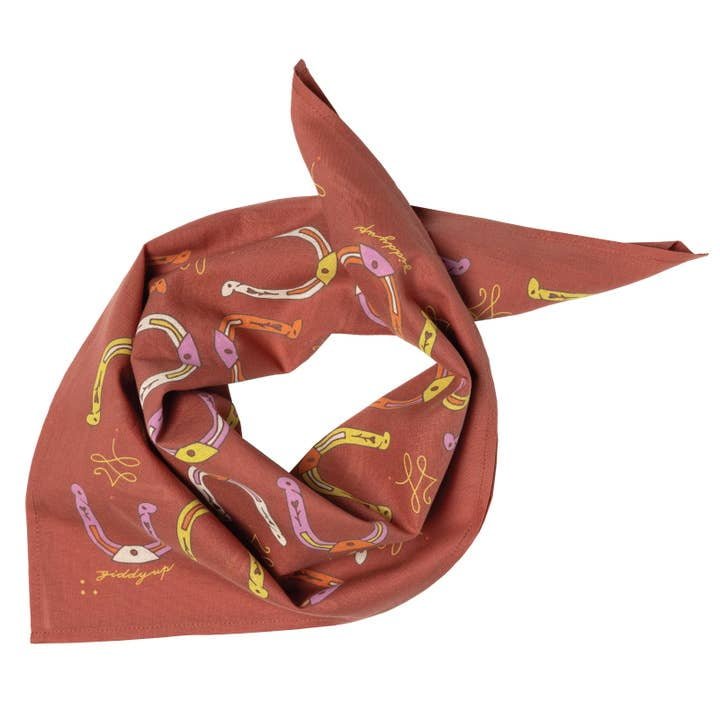 The "Giddy Up" bandana by Jenni Earle features a rust color with stylized yellow, pink, and purple horseshoes and farrier nails—a unique accessory or uplifting gift.