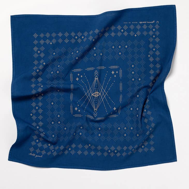 The "Hell Yeah" bandana by Jenni Earle is a western-style blue accessory with gold geometric patterns, lines, an eye motif at the center, and decorative borders. Made in the USA.