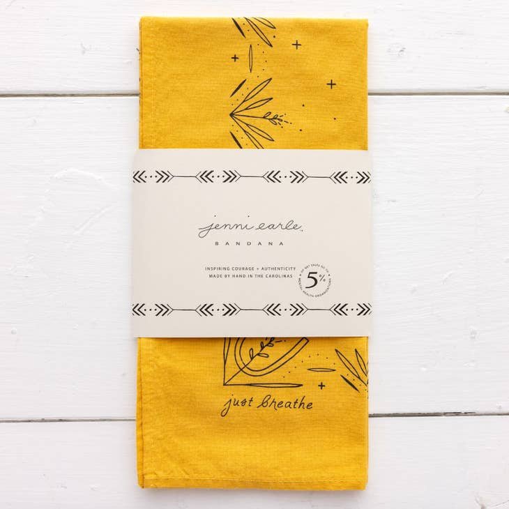 A hand-dyed yellow "Just Breathe" bandana by Jenni Earle features simple black line designs, wrapped in a branded white paper band. This unique western style accessory is proudly made in the USA.