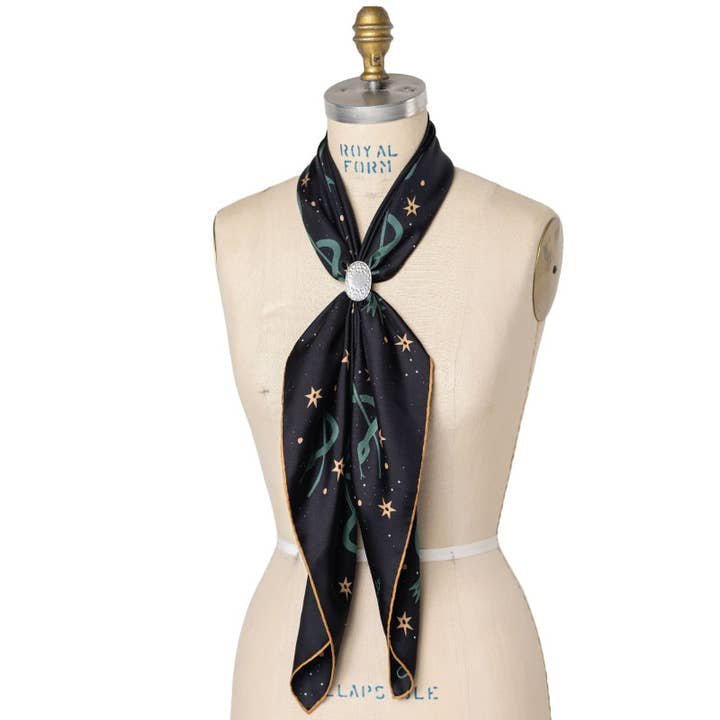 The Jenni Earle "Lasso The Stars" Bandana, featuring a star pattern, is elegantly tied around a dress form’s neck with a brooch—an ideal gift or luxury accessory for those seeking Jenni Earle’s signature style.