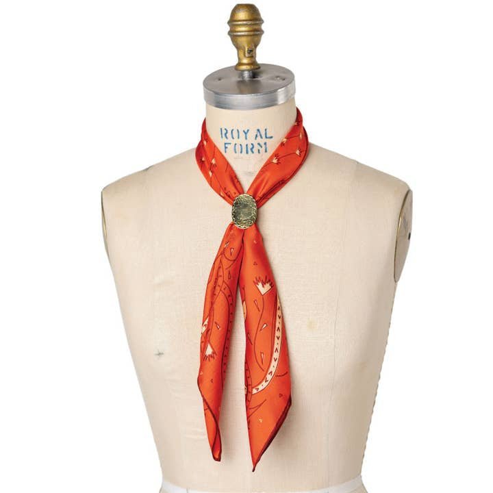 A mannequin showcases the Jenni Earle Bandana | Own Your Power Silk in orange, styled with a decorative pin—a sophisticated pick for silk scarf lovers or a festive holiday gift.