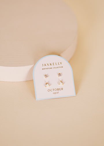 A card labeled "Birthstone Earrings | JaxKelly" features a pair of opal stud earrings with hypoallergenic sterling silver posts, displayed on a beige surface.