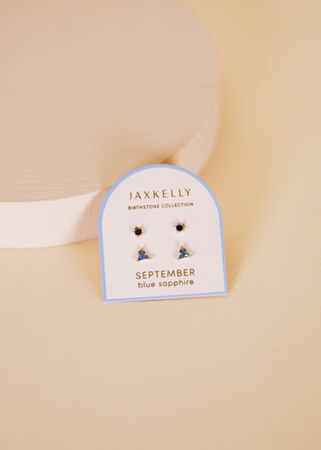 JaxKelly Birthstone Earrings with blue sapphire stones and hypoallergenic sterling silver posts are displayed on a "Birthstone Collection, September" card against a beige background.