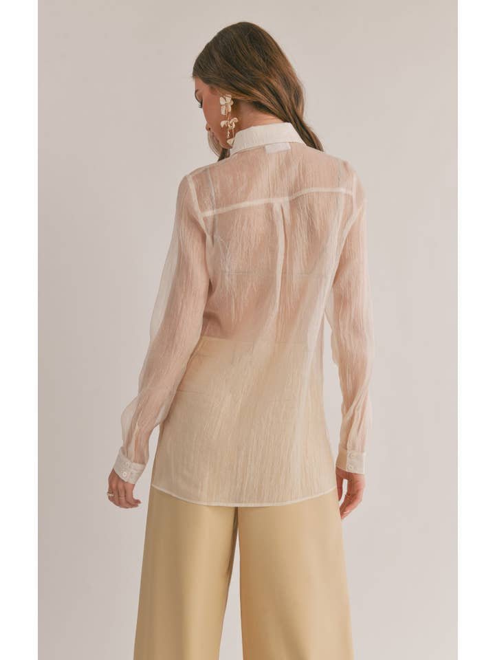 A woman faces away, wearing Sage the Label's Blurred Sheer Button Down Shirt in Butter, paired with beige wide-leg pants against a neutral background.
