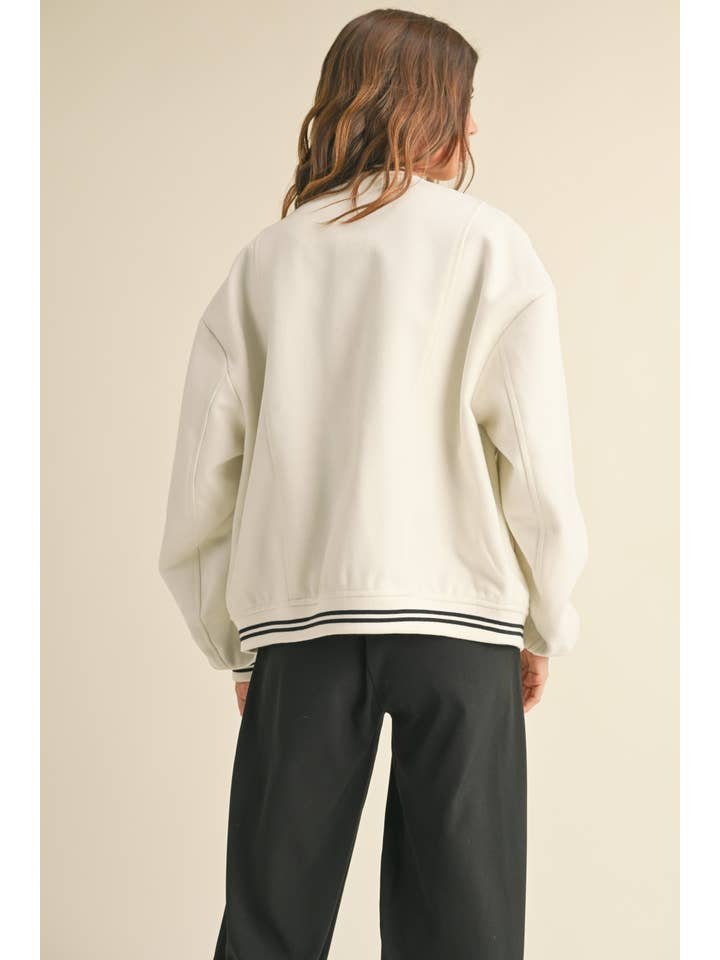 A person with light brown hair, seen from behind, wears the Miou Muse Bomber Jacket in white with black striped trim and pairs it with black pants.