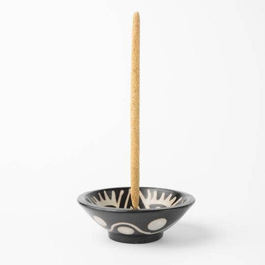 The Chulucanas Ceramic Incense Holder Modelo Clasico by Luna Sundara, a black ceramic bowl with white patterns, holds a vertical incense stick against a plain white background.