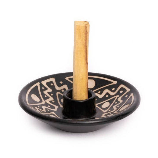 The Chulucanas Ceramics Palo Santo Holder by Luna Sundara is a black ceramic piece with beige geometric patterns, handmade by Peruvian artisans, and holds a central wooden stick upright.