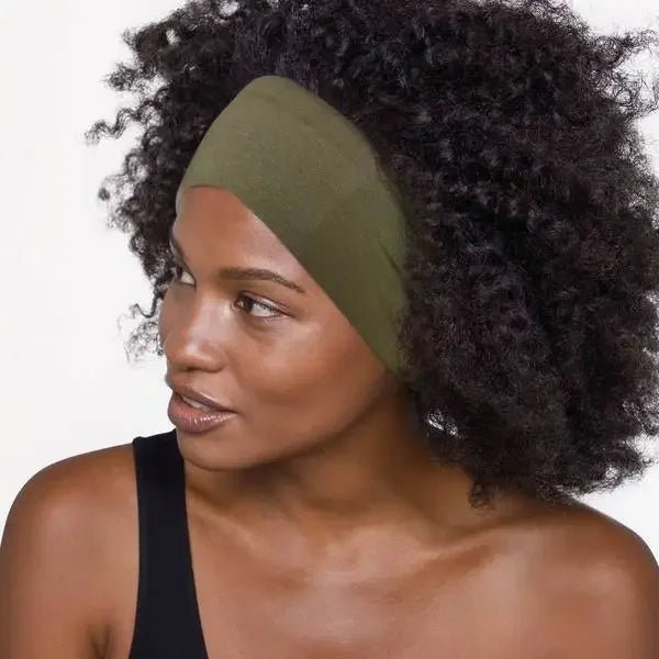 A woman with curly hair wears a KITSCH Cotton Adjustable Headband 2pc in eco-friendly olive green and a black top, looking to the side against a plain background.