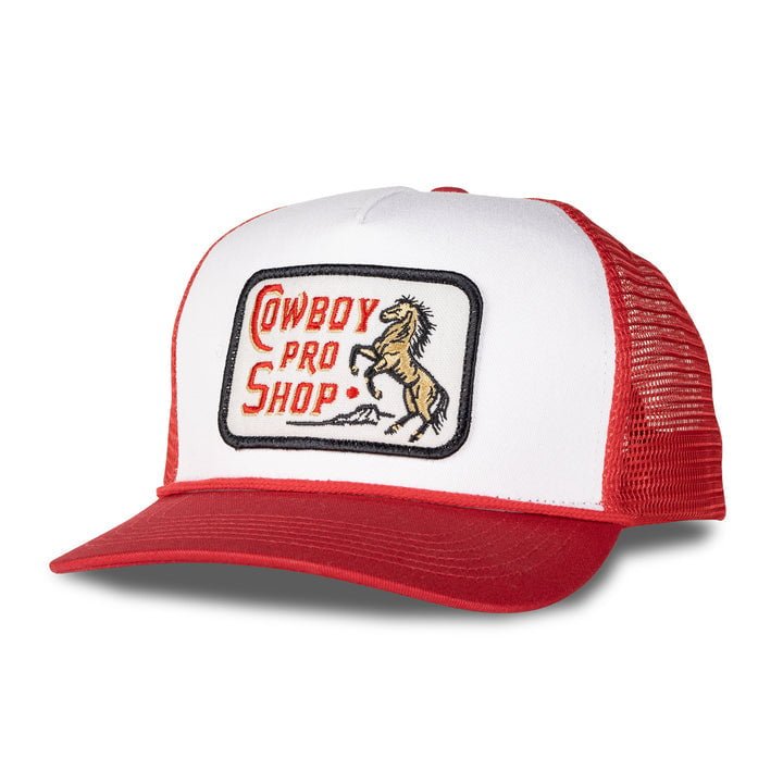 The Cowboy Pro Shop Hat by Sendero Provisions Co. is a red and white trucker cap with mesh back and a "Cowboy Pro Shop" patch with a rearing horse—ideal for road trips or sharing laughs at the rodeo.