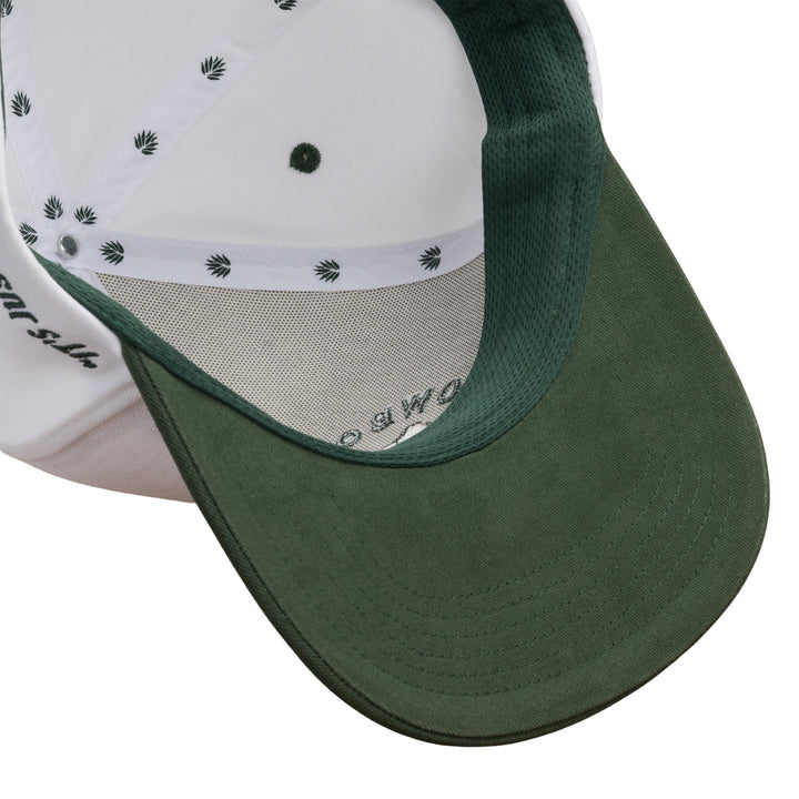 A close-up of the Cowboys Don't Cry Hat by Sendero Provisions Co.—a baseball cap with a green brim and white interior featuring a small repeating leaf pattern, inspired by classic cowboy style.