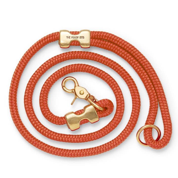 The Foggy Dog | Dog Leash: A coiled orange leash crafted from double-braided marine rope with solid brass hardware, featuring a clasp, ring, and an engraved connector labeled "THE FOGGY DOG.