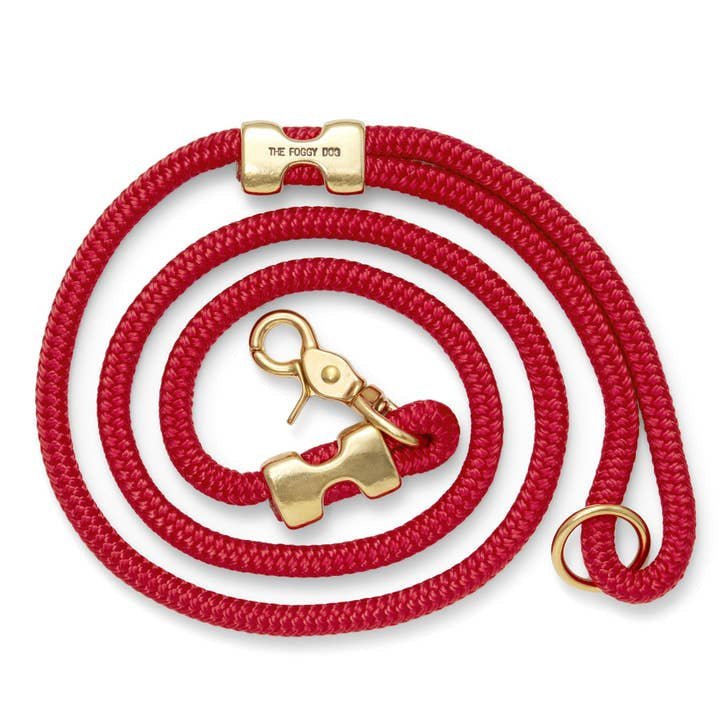 The Foggy Dog Leash is a coiled red dog leash made from double-braided marine rope with solid brass hardware, including a clasp, ring, and connector engraved with "The Foggy Dog.