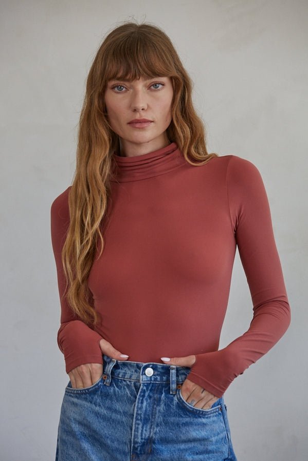 A woman poses for a picture in the Done For Me Bodysuit by By Together, showing off its sleek, seamless design.