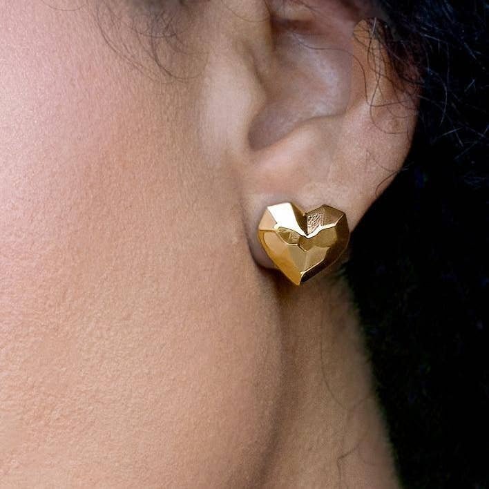 A close-up of a person’s ear wearing Peter and June’s Sweet Disco Stud earrings—18k gold plated, geometric heart-shaped studs crafted from ethically sourced materials.