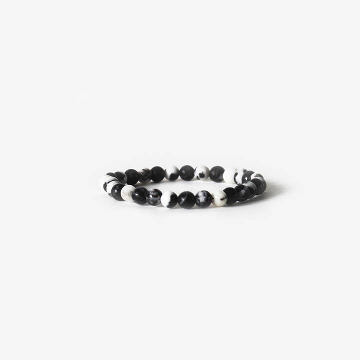 The Earth Bracelet - Zebra Jasper by BRANCO showcases alternating black and white round beads in a single strand, displayed on a plain white background. This gemstone bracelet adds natural style to any outfit.