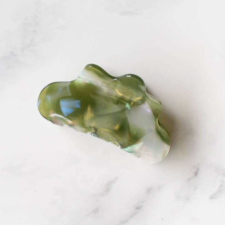 The Eco Cloud Hair Claw Clip by Tiepology, a green pearlescent accessory, rests on a white marble surface—an eco-friendly and whimsical hair clip.