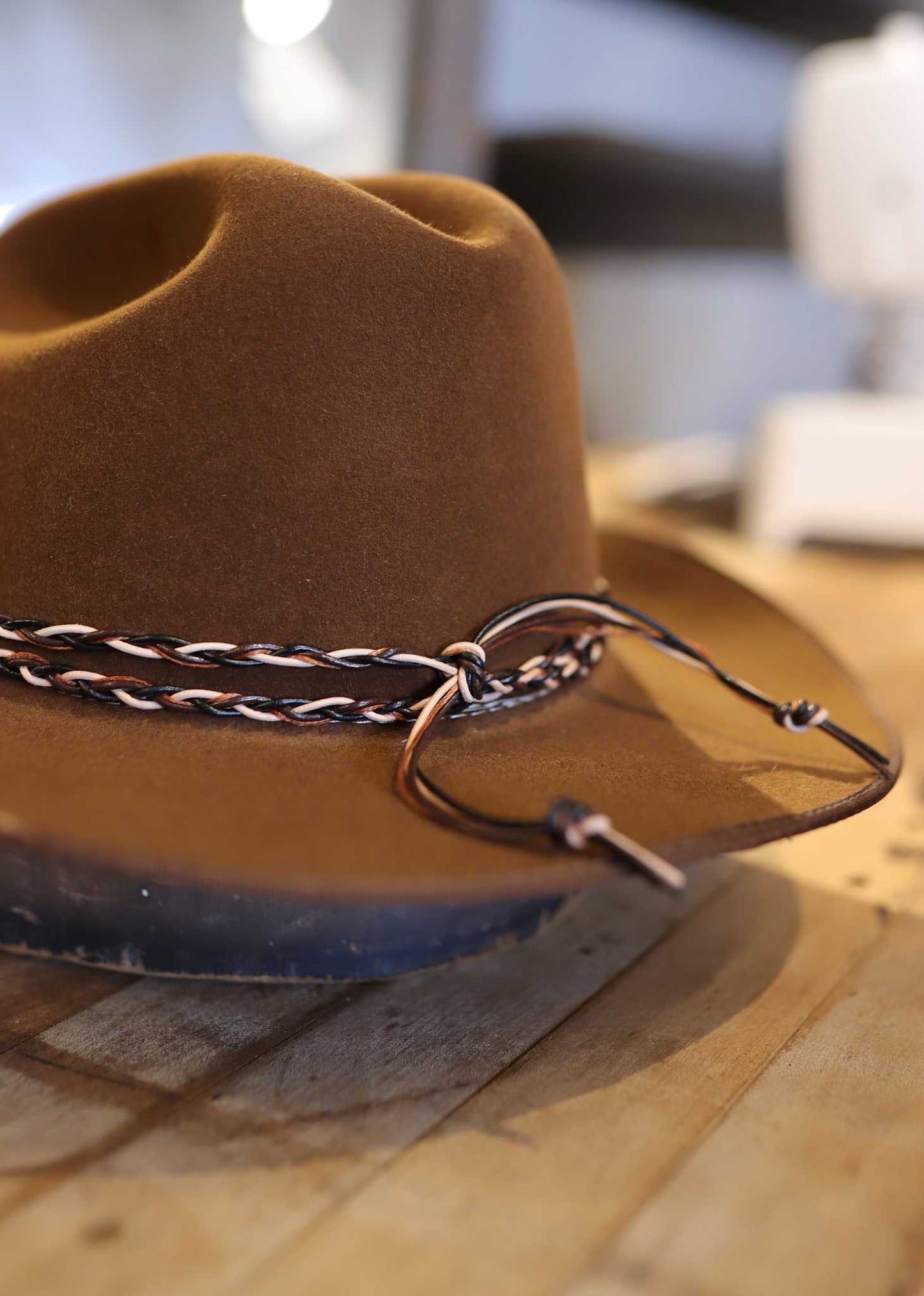 The Easy Drifter Felt Hat | Whiskey LBJ features a braided leather band and sits on a wooden surface.