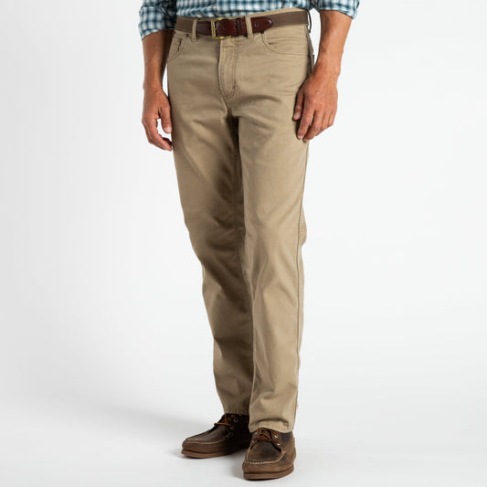 A man wears Duck Head Field Canvas Five-Pocket pants, styled with a brown belt, plaid shirt, and brown boat shoes, standing against a plain white background.