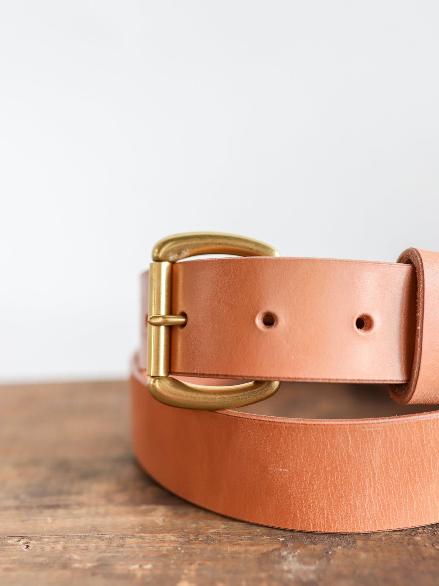 A close-up of the Ballad of the Bird Dog Field Duty Belt, featuring a gold buckle and vegetable tanned Wickett & Craig harness leather, shown resting on wood against a plain white background.