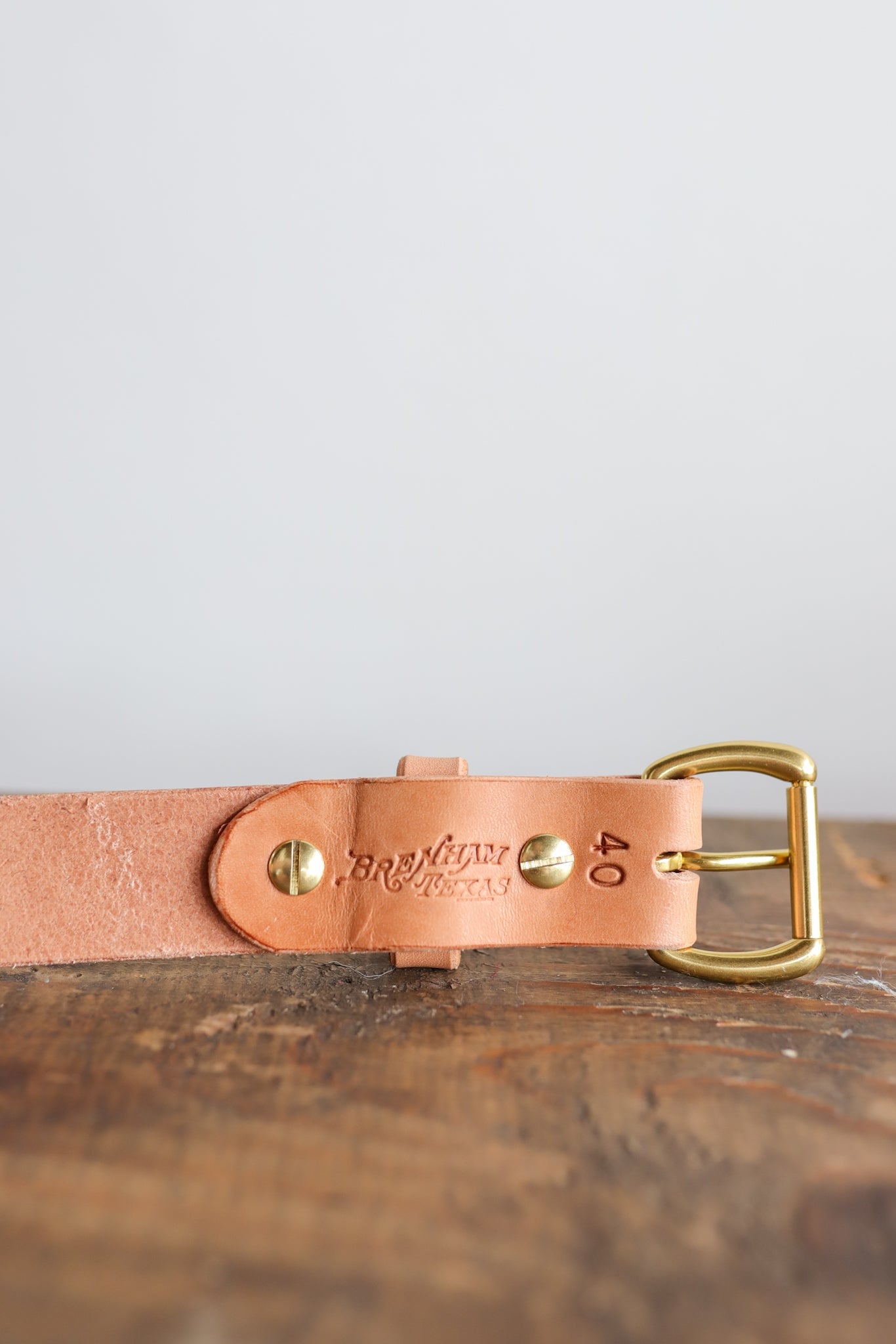 A close-up of the Ballad of the Bird Dog Field Duty Belt, featuring embossed branding and the number 40 on Wickett & Craig harness leather with a brass buckle, resting on a wooden surface.