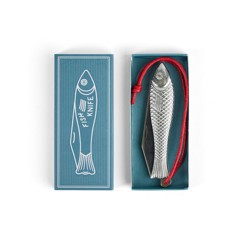 The Fingerling Fish Knife by Mollyjogger features a fish-shaped chrome handle, stainless blade, red cord, and comes in an open box next to packaging with a fish illustration labeled "Fish Knife." A unique collector's item for cutlery enthusiasts.