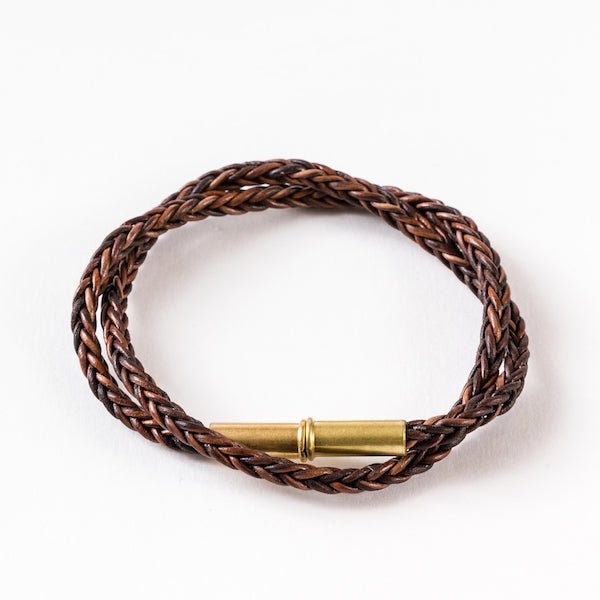 The Flint Braided Bracelet by Tres Cuervos features upcycled .22 shells and a magnetic clasp, shown coiled on a white background.