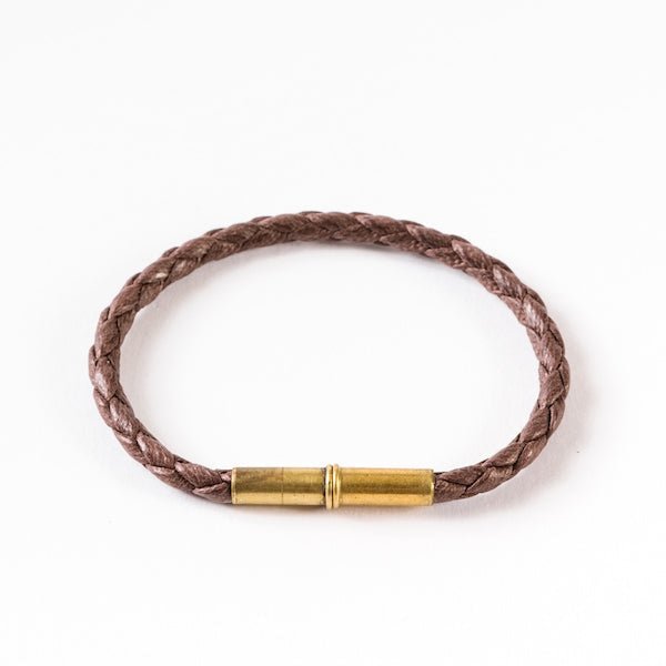 The Flint Single Waxed Canvas Bracelet by Tres Cuervos features a brown braided leather band with a cylindrical brass magnetic clasp, elegantly displayed on a white background.