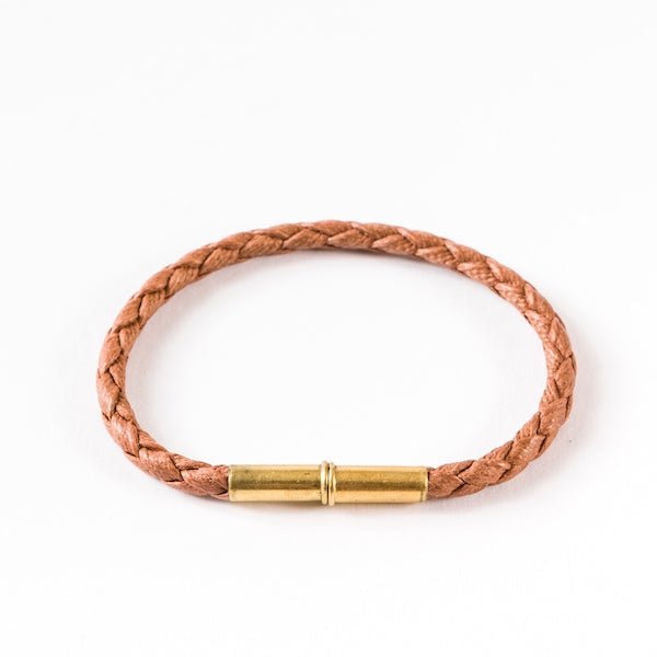 The Flint Single Waxed Canvas Bracelet by Tres Cuervos features a brown braided design with a gold cylindrical magnetic clasp, showcased on a plain white background.