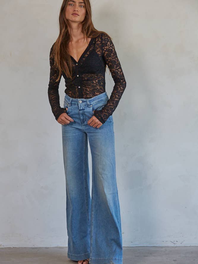 Woman standing against a plain wall, wearing the By Together Floral Lace Bodysuit.