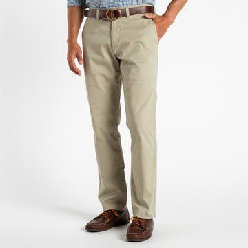 A man wearing Duck Head's Gold School Chino (Big Gold Patch), a brown belt, brown shoes, and a patterned shirt stands against a white background, showcasing the brand's classic American style.