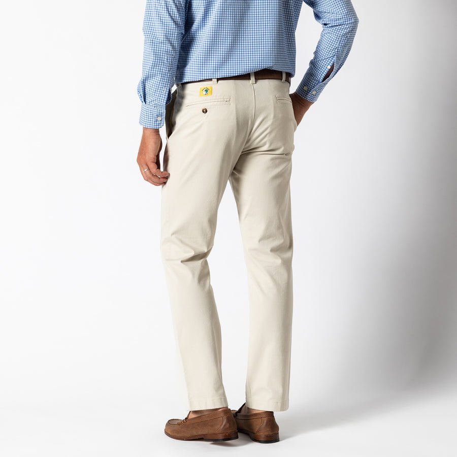 A person in a blue checked shirt, brown shoes, and beige Gold School Chino (Big Gold Patch) pants by Duck Head stands facing away from the camera against a plain white background.