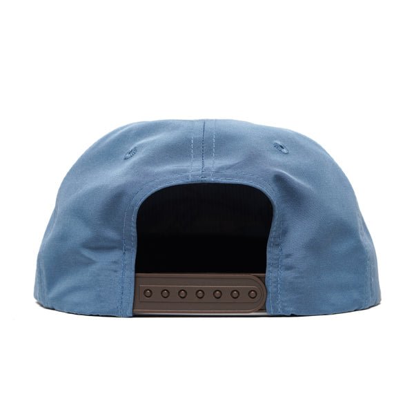 The Grandpa Hat | Redfish by Duck Camp is a blue adjustable cap, shown from the back, with a brown plastic embroidered snapback closure.