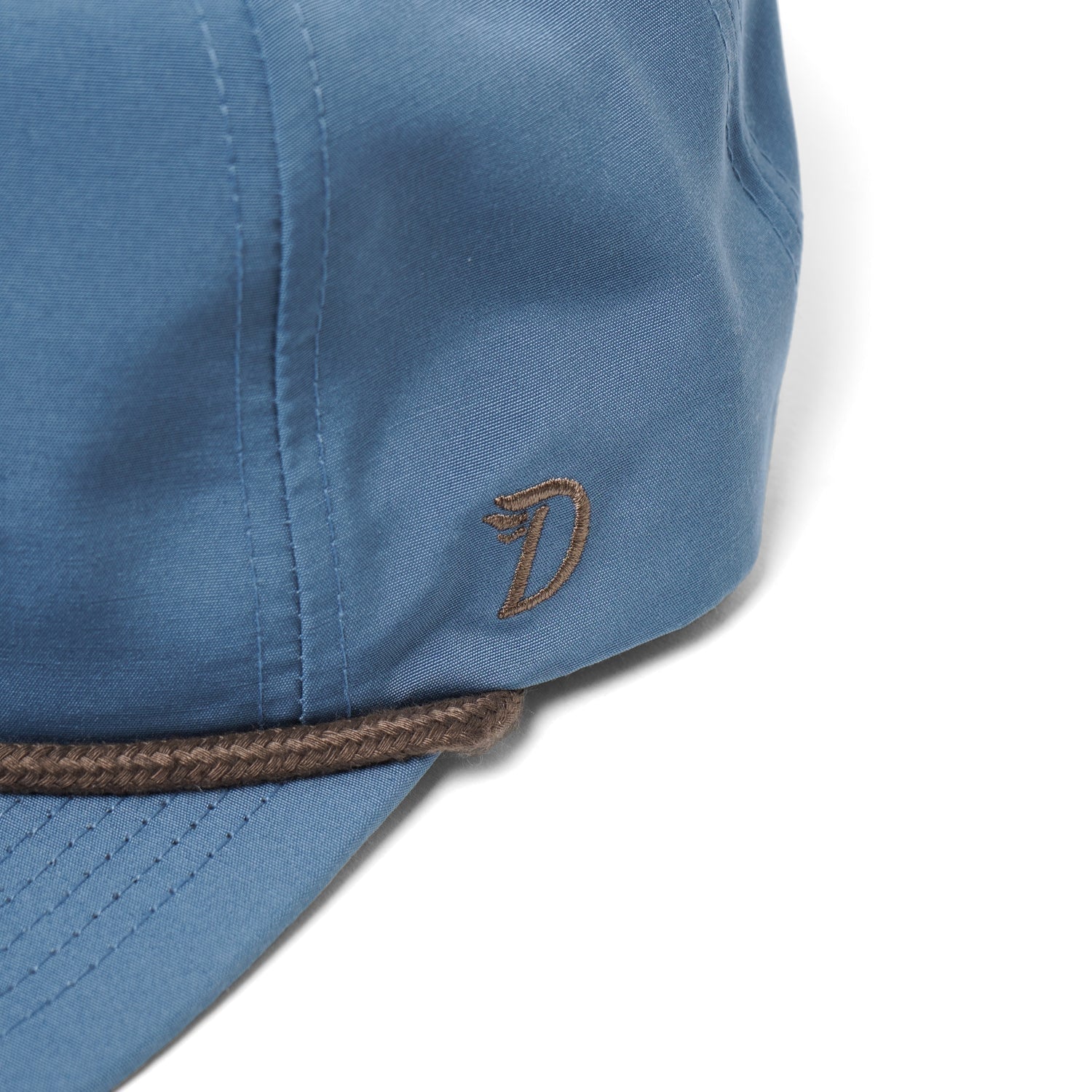A close-up of Duck Camp's Grandpa Hat | Redfish, an adjustable blue cap with a brown embroidered "D" and brown braided trim above the brim.