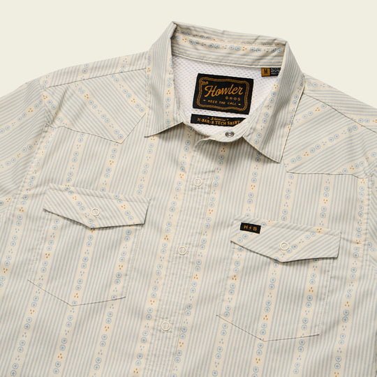 The H Bar Tech Long Sleeve in Mosquero Stripe by Howler Brothers features light gray and blue stripes, two front pockets, stretch nylon-poly fabric, UPF 35 sun protection, and a chest logo tag.