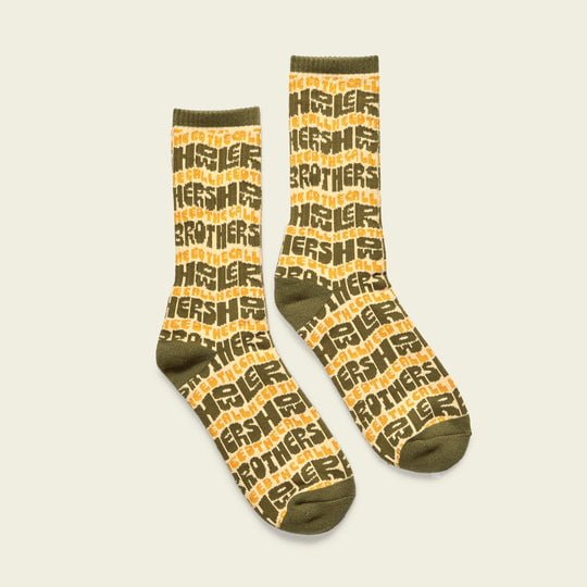 A pair of olive green and yellow HB Flow athletic crew socks by Howler Brothers, featuring a vintage-inspired design and a repeating “Howler Brothers” block-letter pattern.
