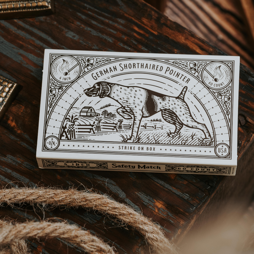 A box of Hounds Safety Matches by Mollyjogger featuring vintage artwork of a German Shorthaired Pointer with countryside scenery, labeled “German Shorthaired Pointer” and “USA.”.