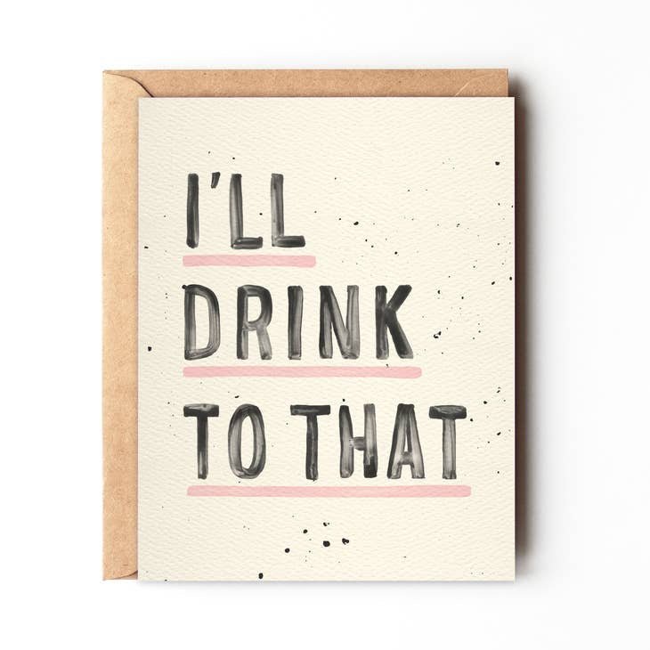 The “I’ll Drink To That” greeting card by Daydream Prints features bold black lettering with pink lines under “DRINK” and “THAT,” making it a fun congratulations card, shown atop a brown envelope.