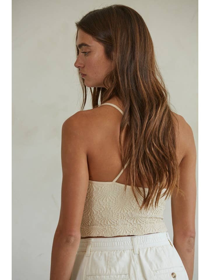 A woman with long brown hair stands with her back to the camera in a cream-colored By Together Knit Modal Nylon Spandex Seamless Jacquard Tank and white pants, set against a light background.