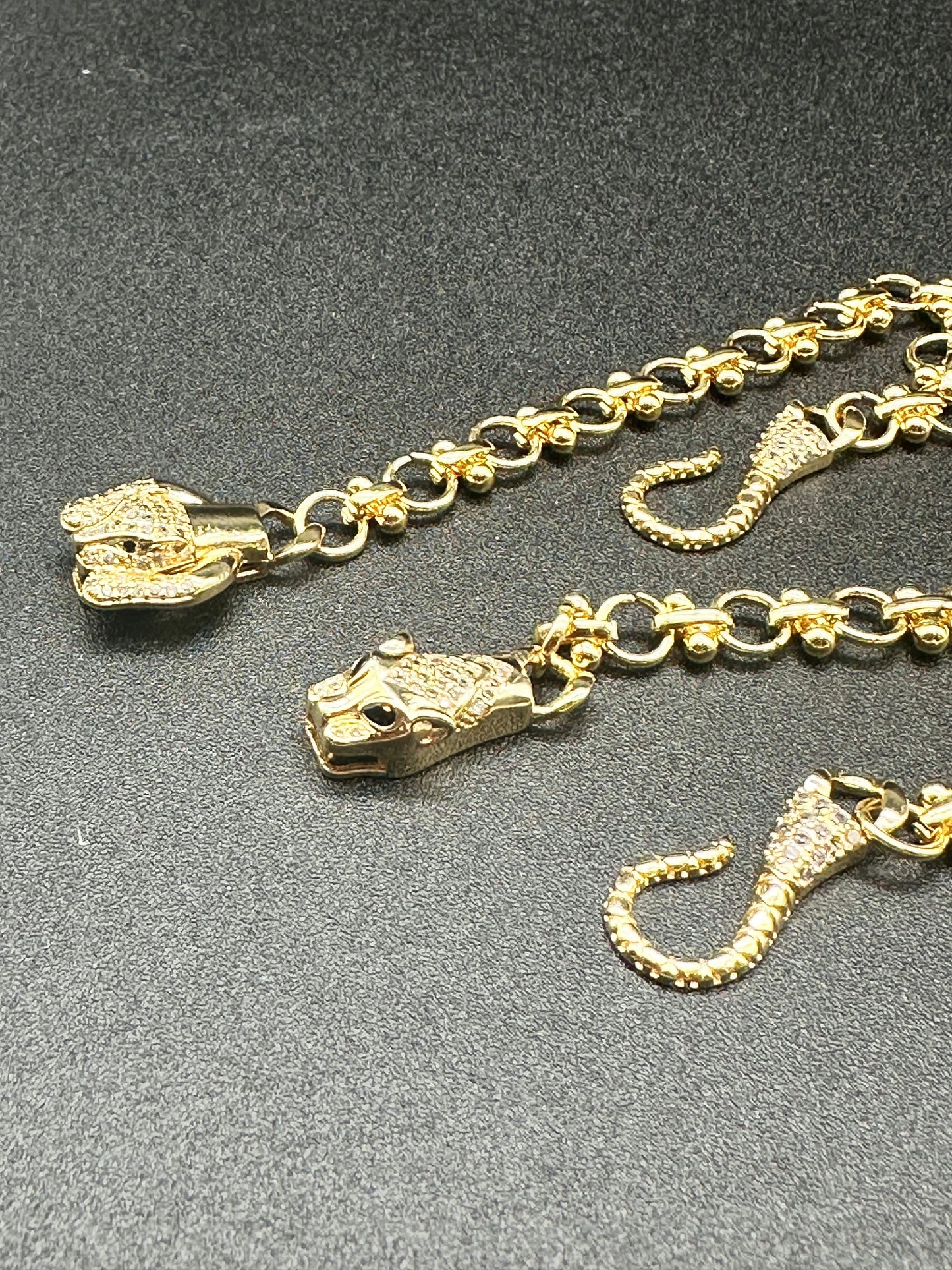 La Prise Bracelet by Minh Atelier: An 18k gold plated chain bracelet featuring panther head and tail charms on a black textured surface—a bold wild cats statement piece.