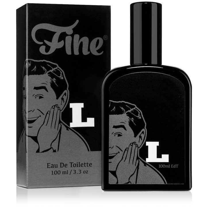 A black 100 ml glass bottle and box of Latigo Eau De Toilette by Fine Accoutrements, with a retro illustration of a smiling man and a large white "L" on both the bottle and packaging—a standout fragrance.