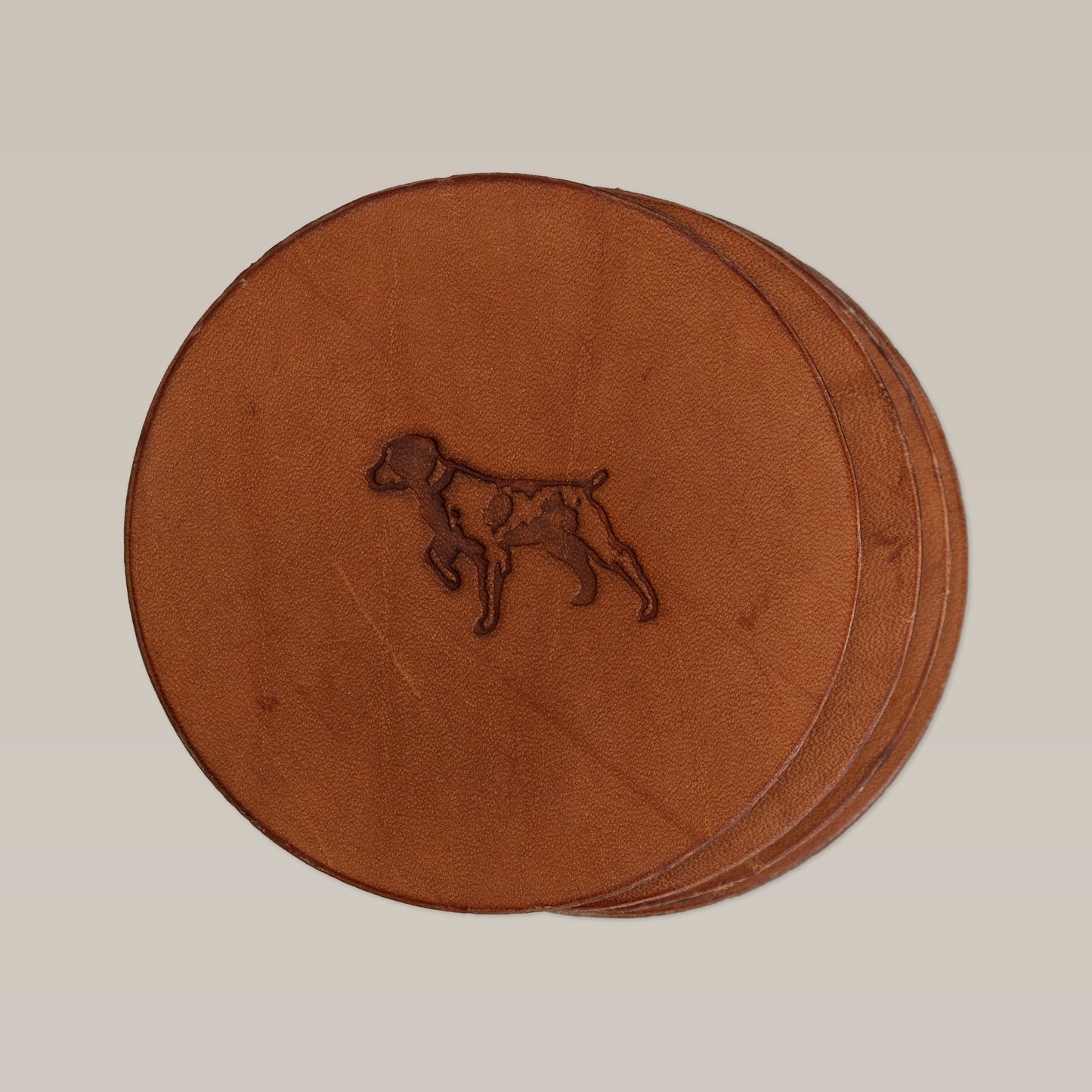 The Leather Coaster 4 Piece Set by Ballad of the Bird Dog features four stacked round leather coasters, the top one embossed with a dog outline, combining style and desk protection in a neutral look.