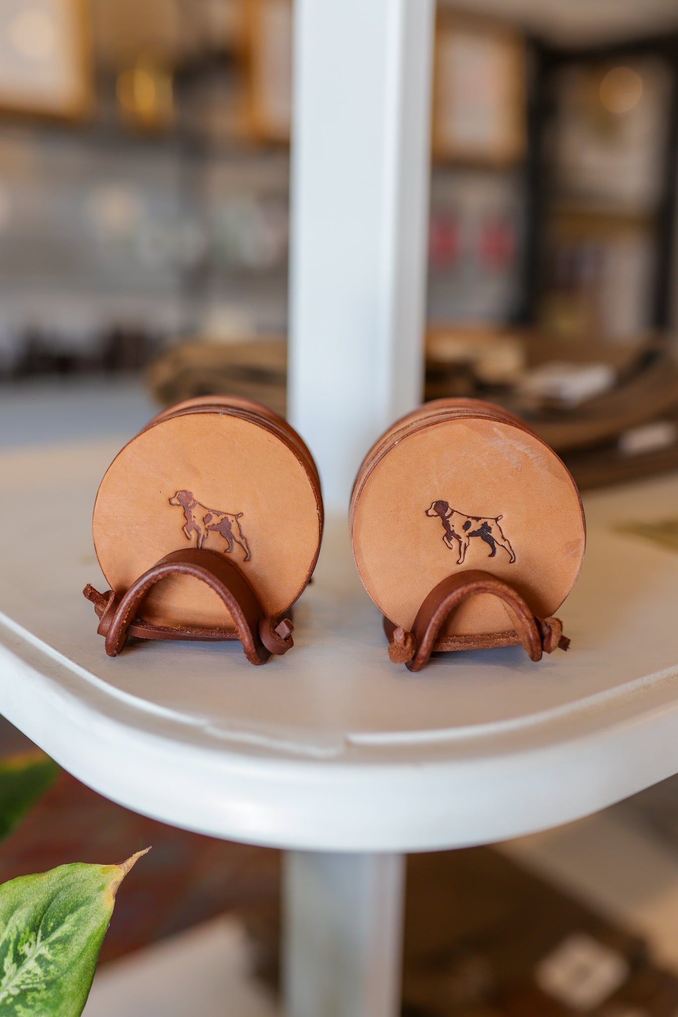 The Leather Coaster 4 Piece Set by Ballad of the Bird Dog features round, brown leather coasters with a dog silhouette, offering stylish desk protection and keeping your space tidy. Ideal for pairing with your favorite handmade leather stand.