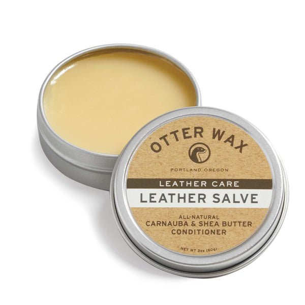 A tin of Otter Wax Leather Salve with the lid partially open reveals smooth, beige salve. The label features carnauba and shea butter, showcasing Otter Wax’s deep conditioning formula for leather care.
