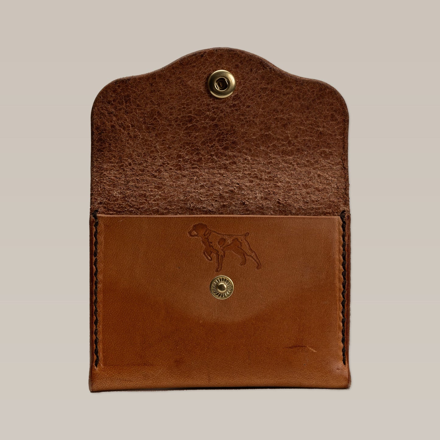 The Ballad of the Bird Dog Leather Wallet is a small card wallet in brown leather with a snap closure. Its front flap features an embossed dog outline and it opens to reveal the interior.