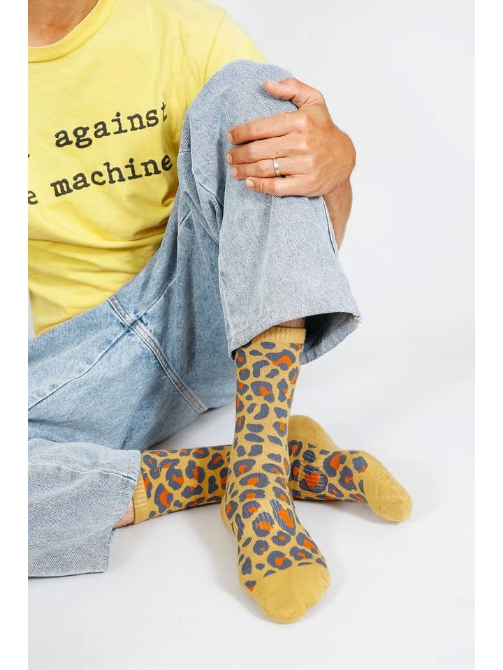 A person wearing light blue jeans, a yellow graphic t-shirt, and Tailored Union's Leo Crew Sock sits cross-legged on the floor.