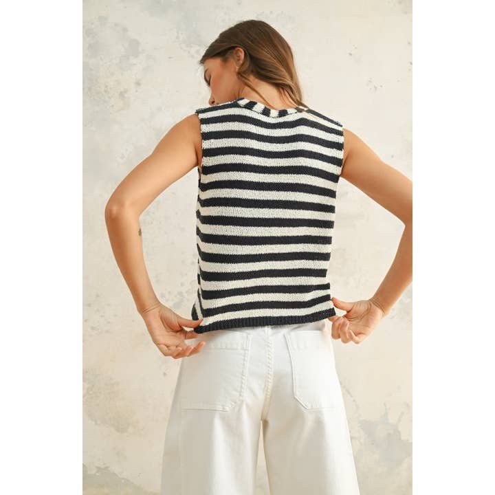 A woman faces away, wearing the Miou Muse Light Weight Hook and Eye Closure Striped Vest in black and white (size S) with white pants, crafted from soft acrylic nylon fabric, set against a neutral background.