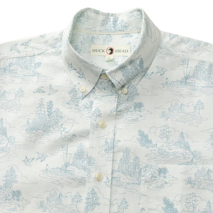 The Duck Head Linen Cotton Oxford Sport Shirt | Lakeview features a light blue and white garment-washed fabric with illustrated outdoor and water scenes, and a "Duck Head" label inside the button-down collar.