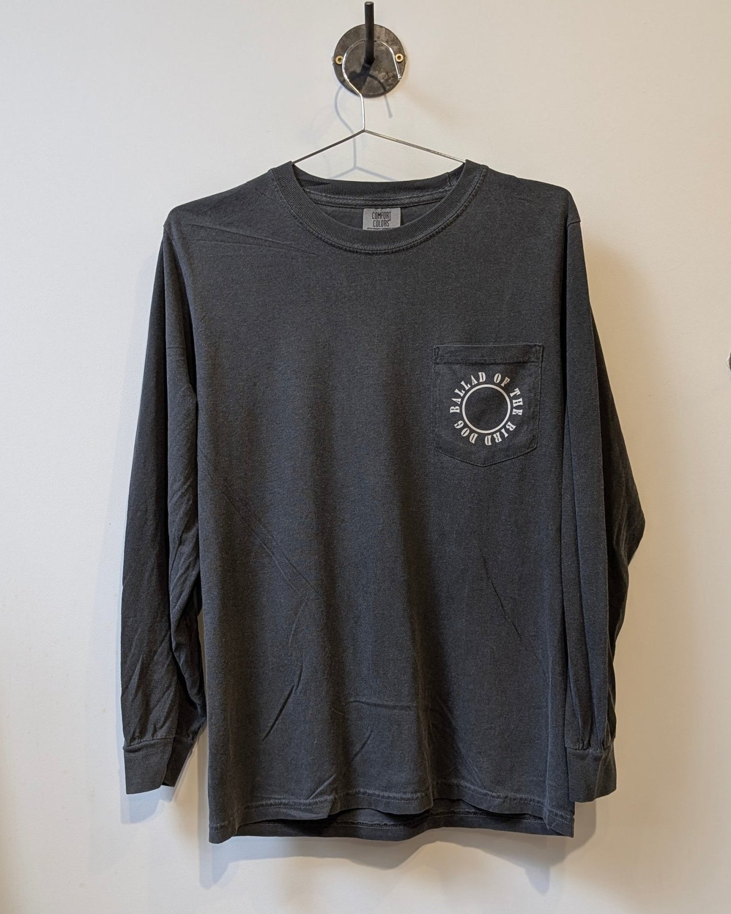 The Ballad of the Bird Dog Long Sleeve Pocket Shirt | Thunderbird features a dark gray design, front pocket, and circular logo with an eye graphic—perfect for any adventure.